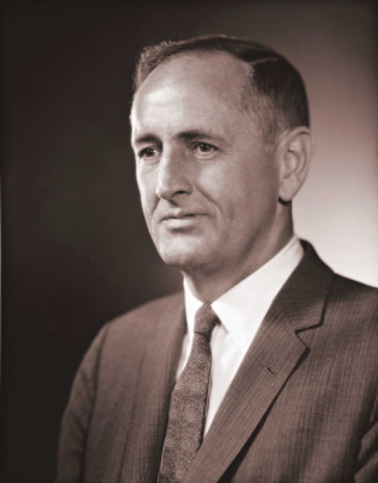 black and white portrait photo of John Gardner in a suit looking off to the left