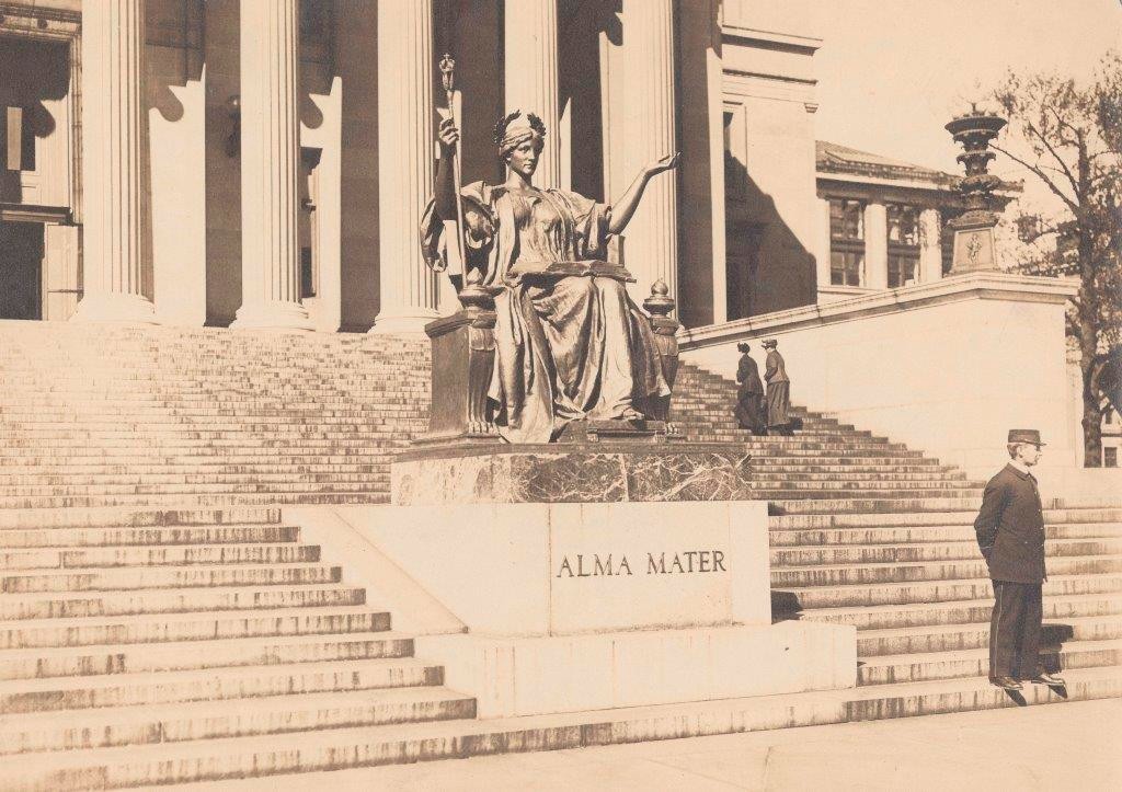 View of Alma Mater in gold leaf with guard standing at her base and two women walking up the stairs to Low Library.